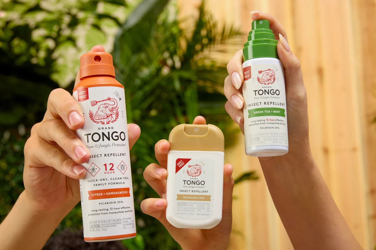 Hands holding Grand Tongo Full Size Spray (4.5 oz), Pocket Spray (1 oz) and Travel Pump Spray (3 oz) in a sunlit backyard