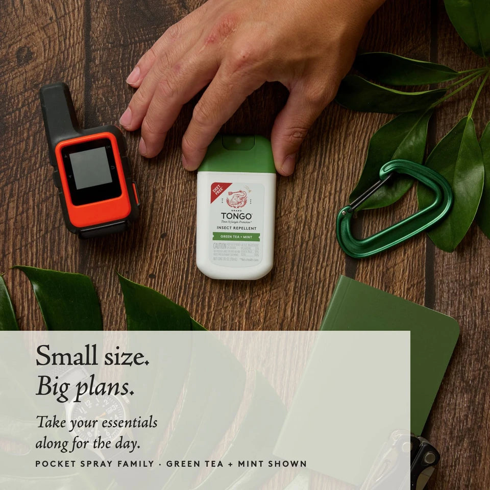 A hand reaches toward Green Tea + Mint Pocket Spray on a wooden table beside outdoor essentials. Small size. Big plans. Green Tea + Mint shown as a Pocket Spray family example.