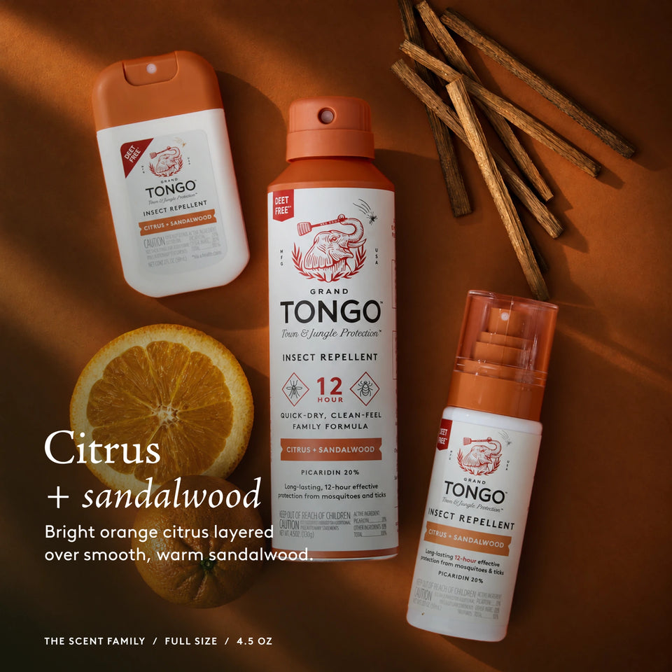 The Grand Tongo Citrus + Sandalwood scent family: full-size, travel, and pocket sprays arranged on orange fabric, citrus, and sandalwood. This is a scent-family image, not the quantity included in the selected product. Citrus + sandalwood. Bright orange citrus layered over smooth, warm sandalwood. The scent family / Full Size Spray / 4.5 oz.