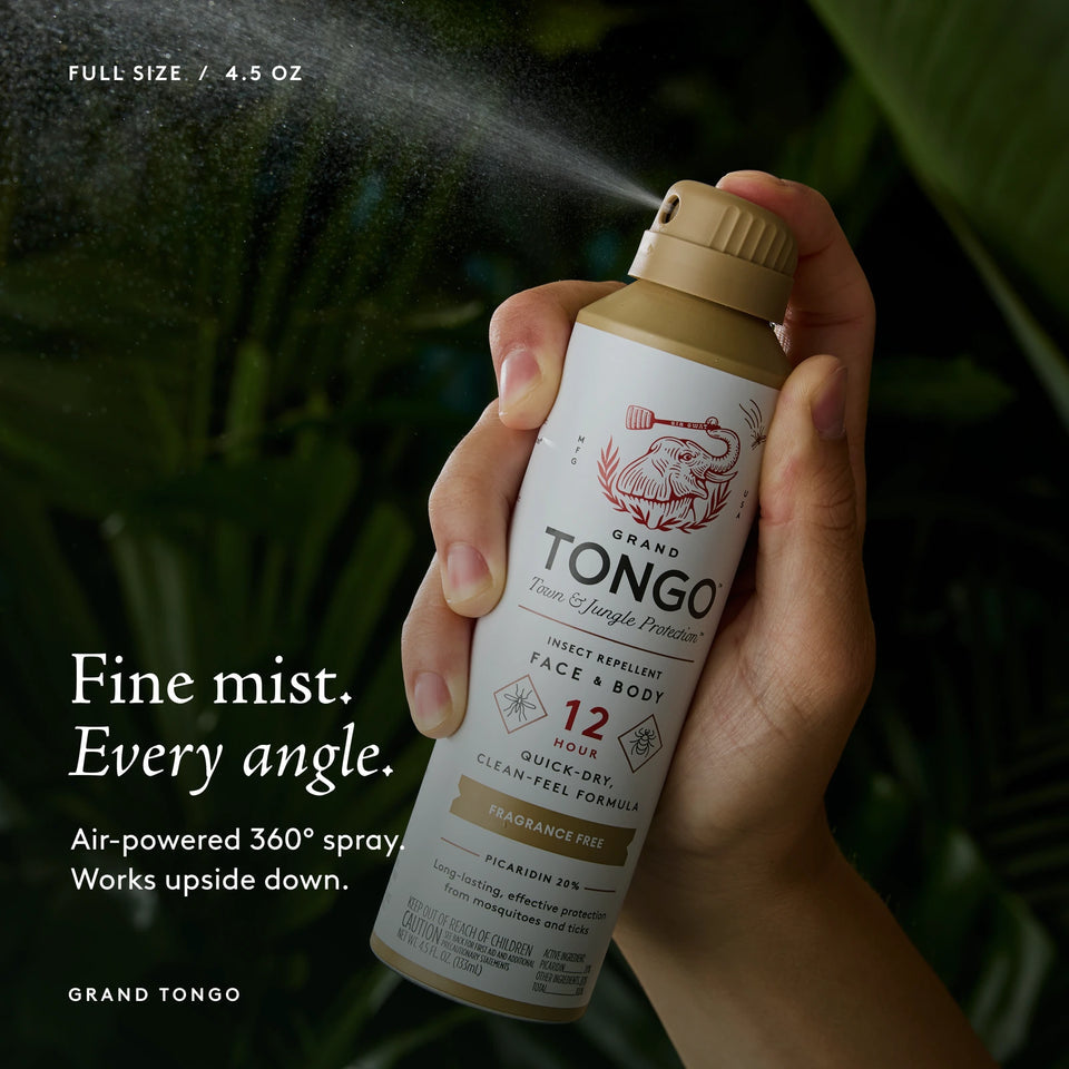 Grand Tongo Fragrance Free Full Size Spray, 4.5 oz held in a hand, dispensing a visible mist against dark green foliage. Fine mist. Every angle. Air-powered 360° spray. Works upside down.