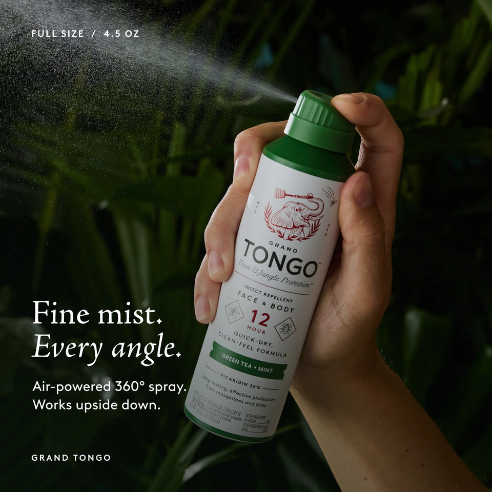 Grand Tongo Green Tea + Mint Full Size Spray, 4.5 oz held in a hand, dispensing a visible mist against dark green foliage. Fine mist. Every angle. Air-powered 360° spray. Works upside down.