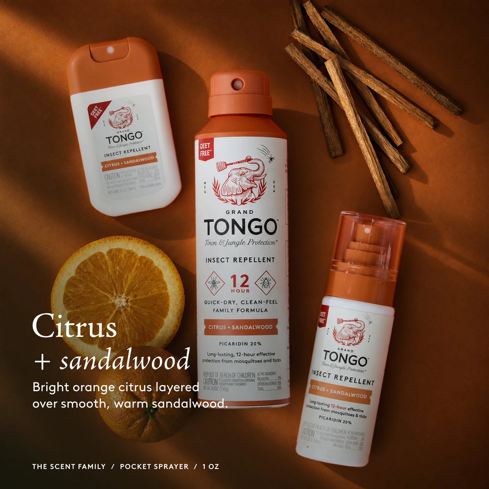 The Grand Tongo Citrus + Sandalwood scent family: full-size, travel, and pocket sprays arranged on orange fabric, citrus, and sandalwood. This is a scent-family image, not the quantity included in the selected product. Citrus + sandalwood. Bright orange citrus layered over smooth, warm sandalwood. The scent family / Pocket Spray / 1 oz.