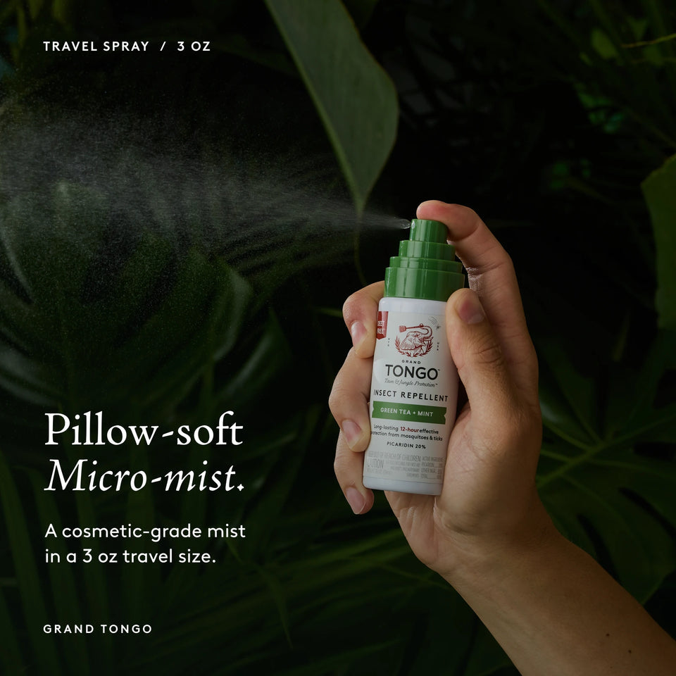 Grand Tongo Green Tea + Mint Travel Pump Spray, 3 oz held in a hand, dispensing a visible mist against dark green foliage. Pillow-soft Micro-mist. A cosmetic-grade mist in a 3 oz travel size.