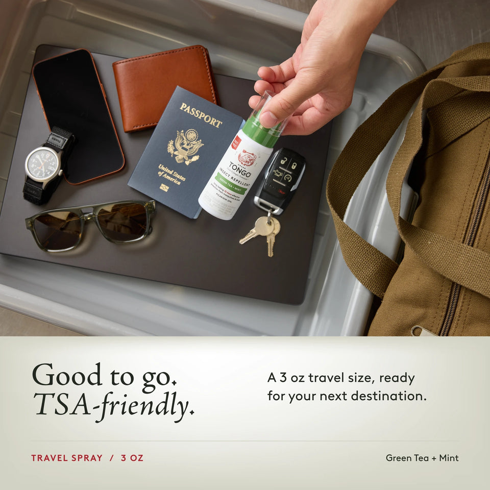 Grand Tongo Green Tea + Mint Travel Pump Spray, 3 oz held over a travel tray alongside a passport, phone, wallet, watch, sunglasses, keys, and bag. Good to go. TSA-friendly. A 3 oz travel size, ready for your next destination.